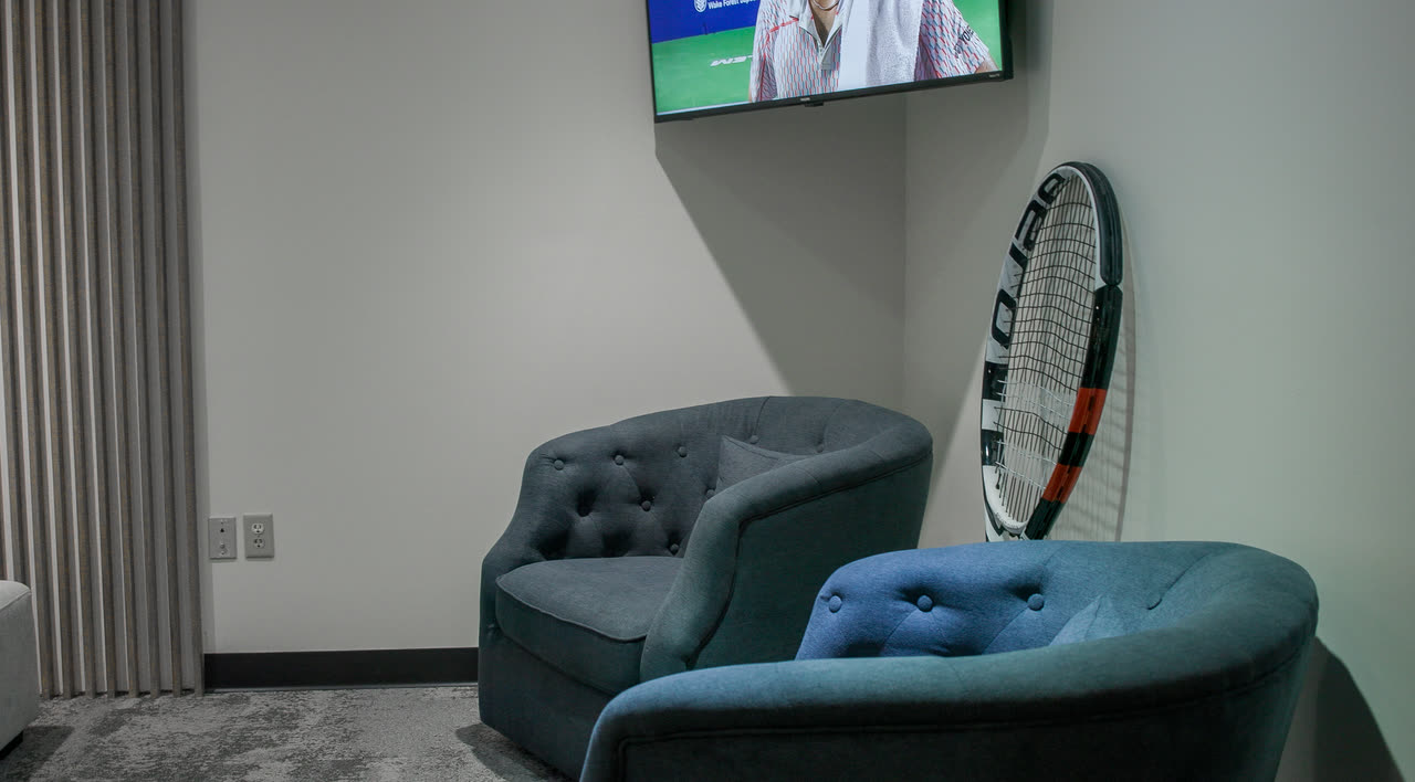 A corner of the lounge at Match Point KC with armchairs and a TV